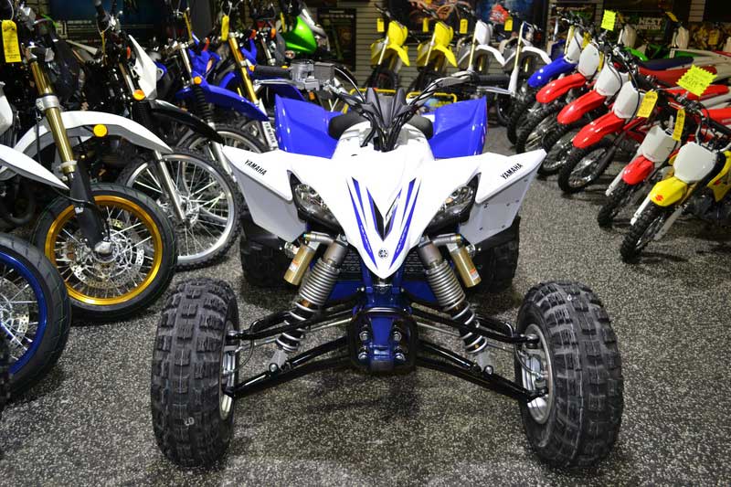 A white and blue Yamaha ATV sitting in a store next to a bunch of dirt bikes