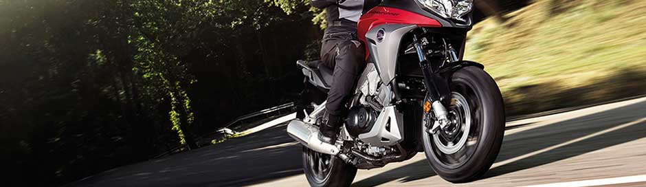 A person riding a red and gray motorcycle down a road next to grass and trees